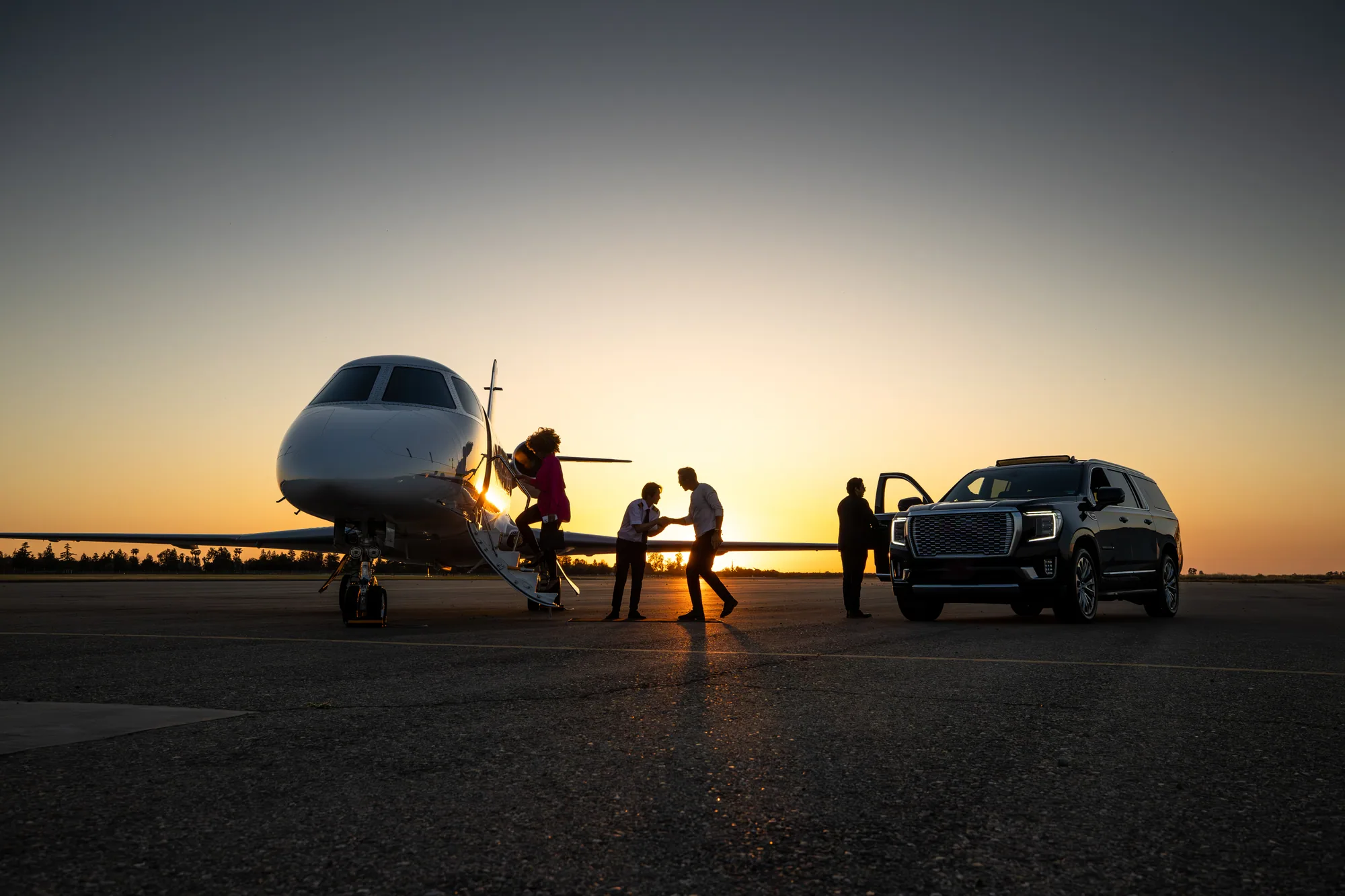 Pilot greeting travelers beside a private jet at sunset