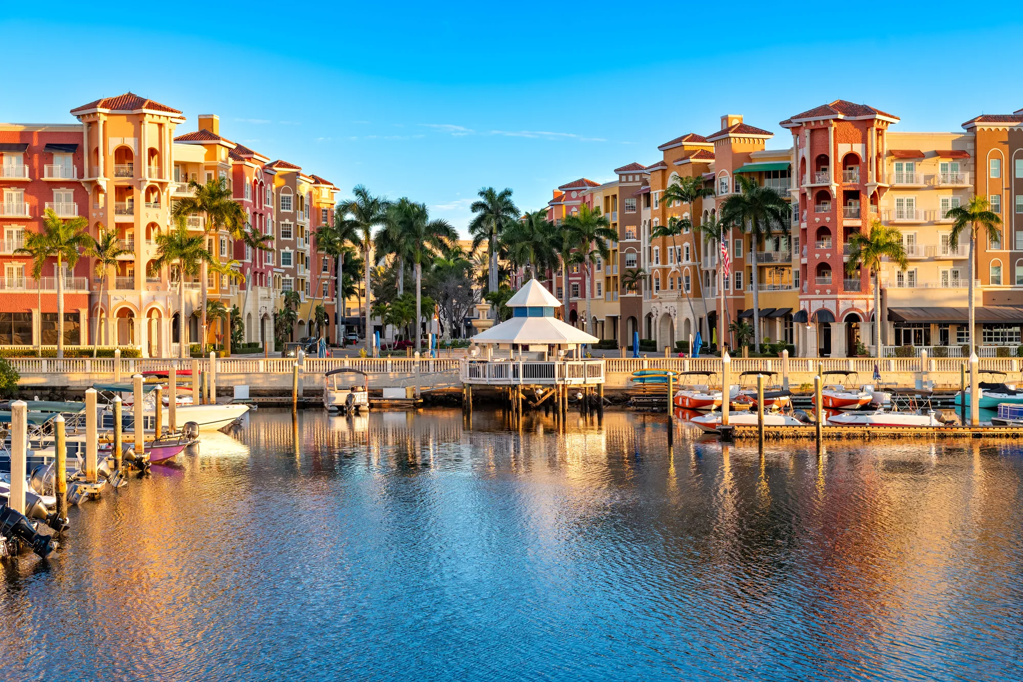 Sunlit waterfront buildings, palm trees and boats in Naples