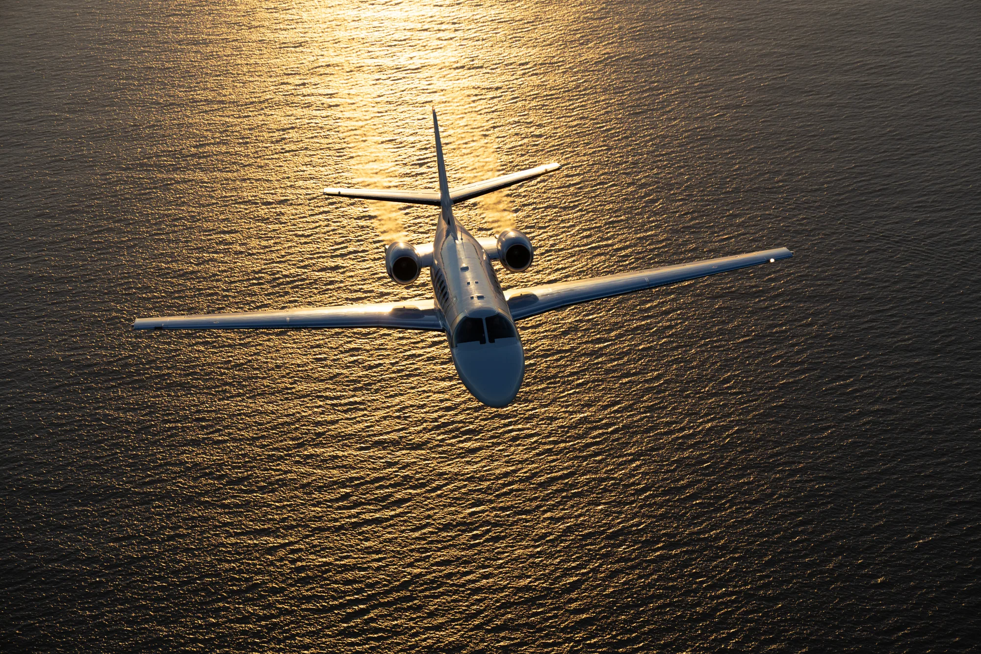 Private jet flying above the ocean in golden evening light